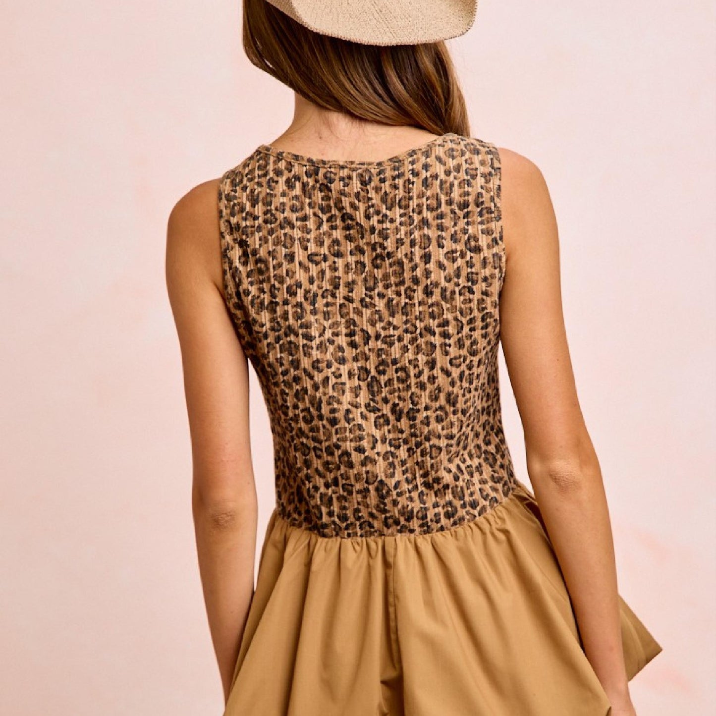 Person wearing a leopard print top and beige skirt on a light pink background