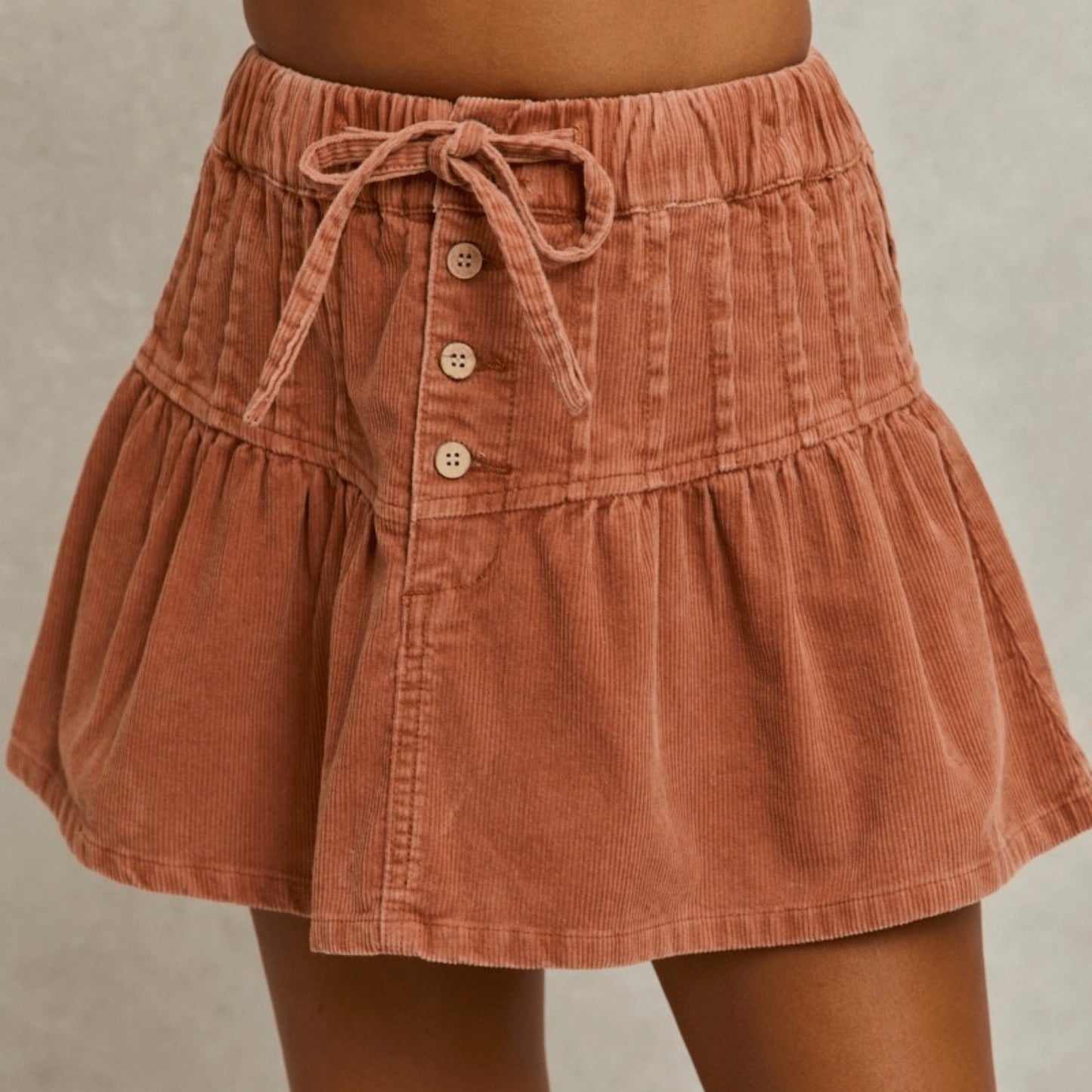 Close-up presentation of the SO ME rust mineral wash corduroy mini skirt with button details.