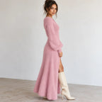 Pink fuzzy knit maxi dress with long sleeves, side button detail, high slit, and white knee-high boots.