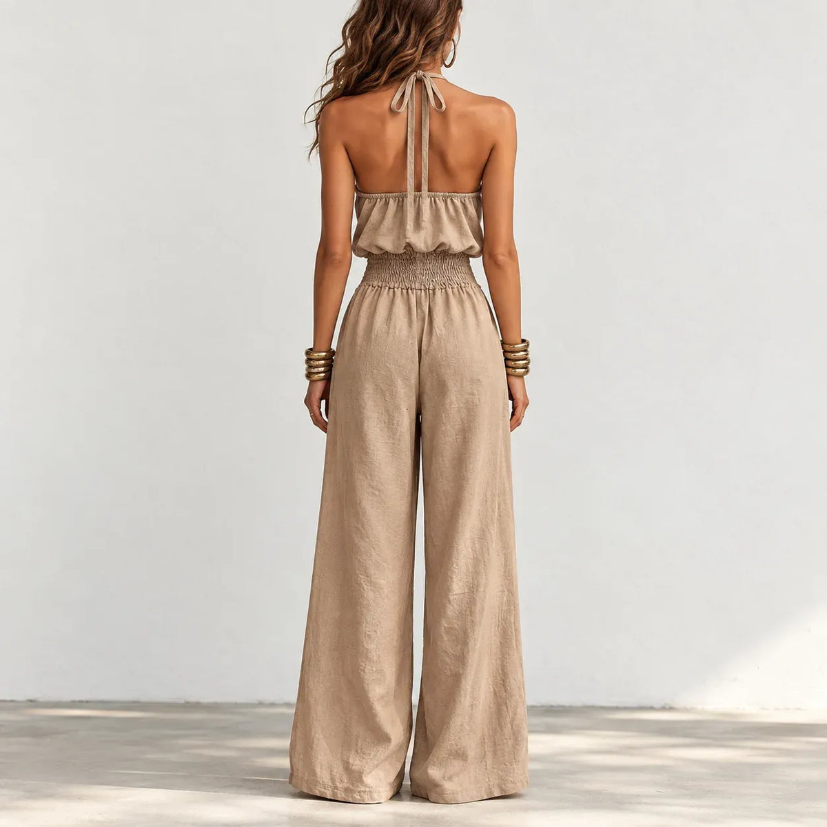 Back view of women’s khaki halter wide-leg linen jumpsuit with halter neck tie and smocked waist