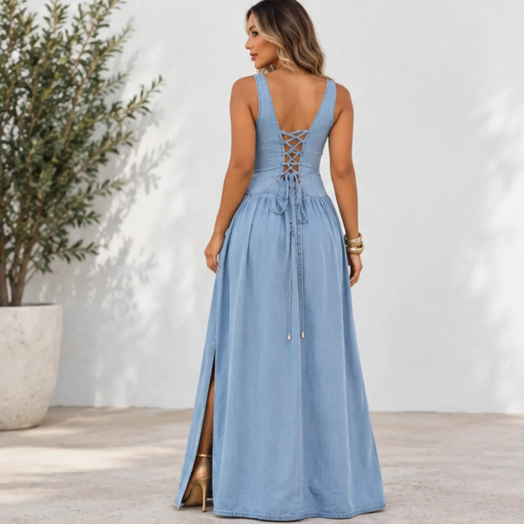 A woman wearing a light blue sleeveless maxi dress with a lace-up open back, shown from the back in an outdoor setting with a white wall and potted plant.