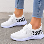 White slip-on knit sneakers with black leopard print details on the sides, shown on a model wearing light blue frayed-hem jeans.