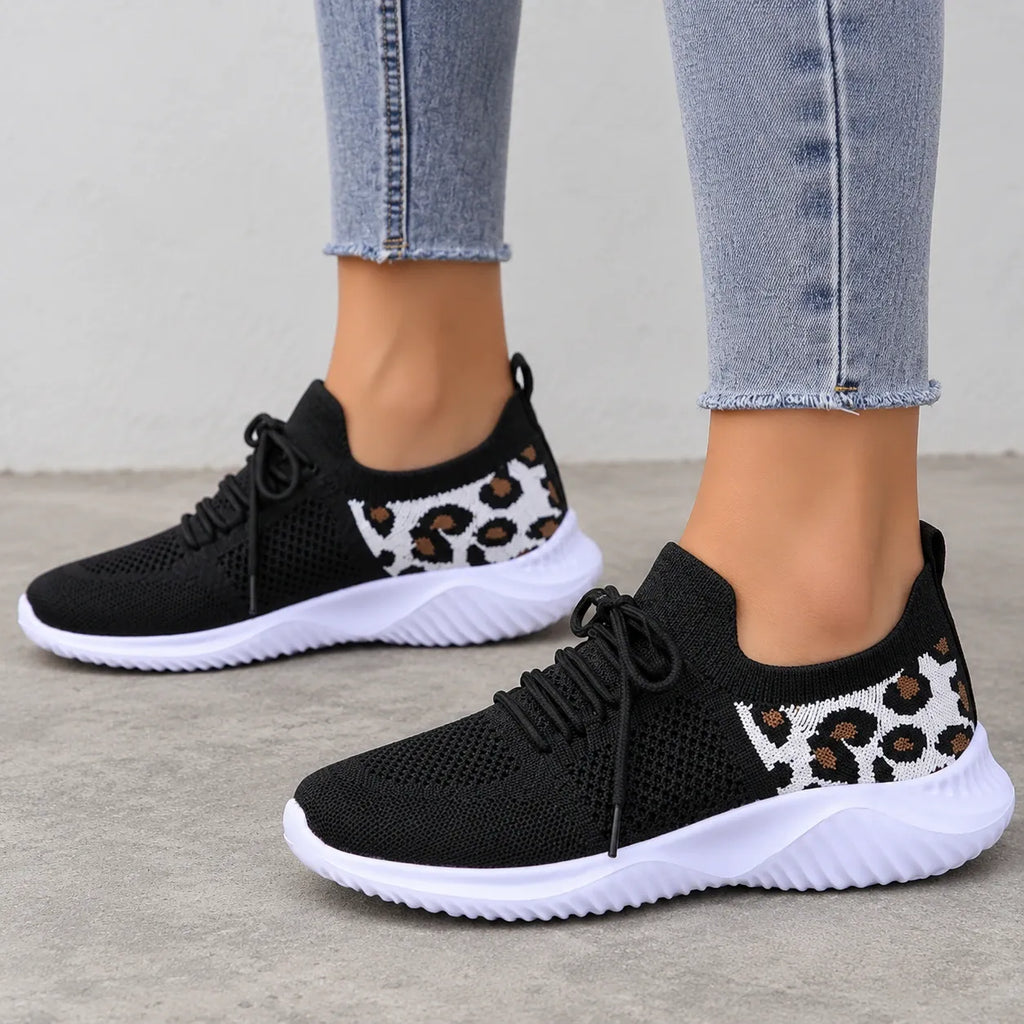 A pair of women's black knit sneakers with white soles and leopard print side panels, shown on a model wearing light-wash frayed-hem jeans.