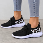 A pair of women's black knit sneakers with white soles and leopard print side panels, shown on a model wearing light-wash frayed-hem jeans.