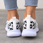 White slip-on knit sneakers with a black leopard print pattern on the heel, shown on a person wearing light blue frayed-hem jeans.