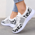 White knit slip-on sneakers with a black leopard print pattern, shown on a model wearing light blue jeans against a neutral concrete wall.