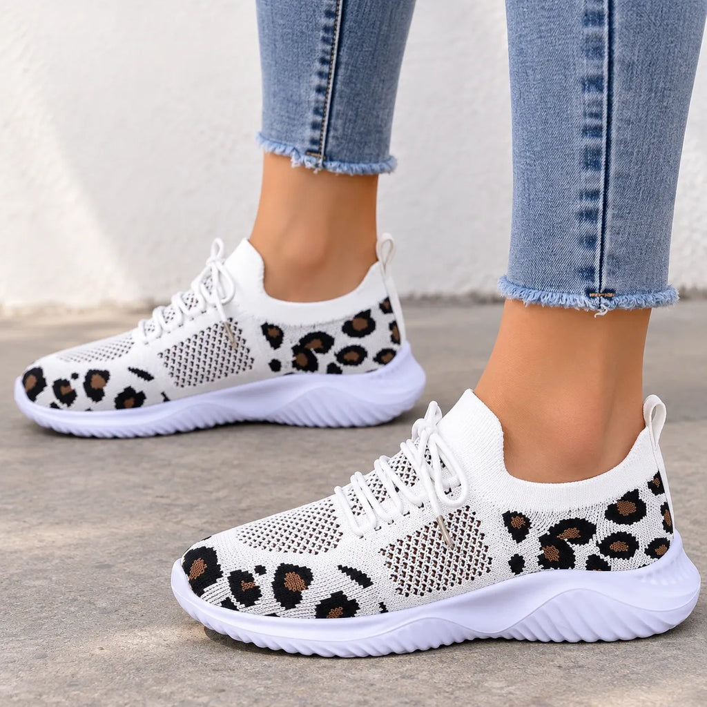 White knit slip-on sneakers with a brown and black leopard print pattern, shown on a model wearing light blue frayed-hem jeans.