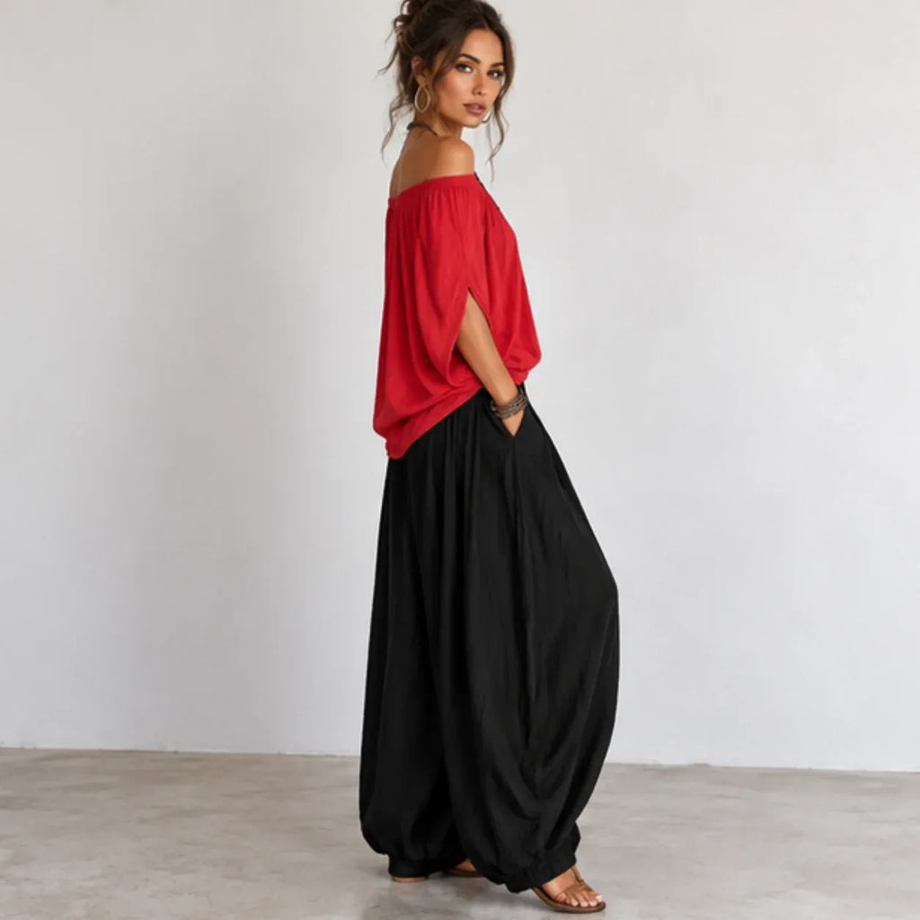 Side view of women’s red and black off-shoulder balloon pants two-piece set with flowing top and relaxed-fit pants