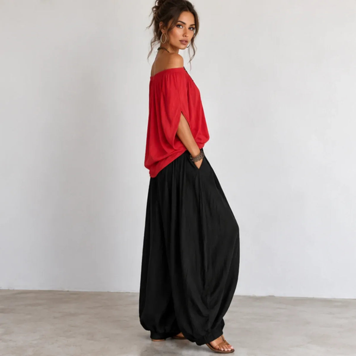 Side view of women’s red and black off-shoulder balloon pants two-piece set with flowing top and relaxed-fit pants