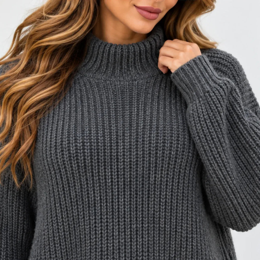 A close-up of a woman wearing a dark gray ribbed knit mock neck sweater, showing the texture of the fabric and her hand adjusting the collar.
