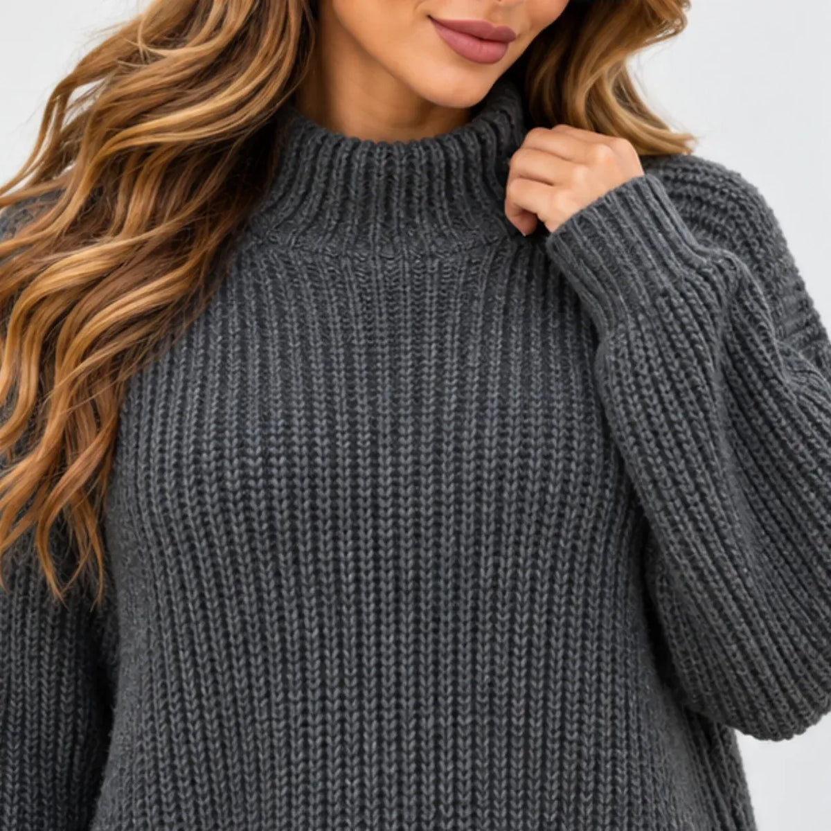 A close-up of a woman wearing a dark gray ribbed knit mock neck sweater, showing the texture of the fabric and her hand adjusting the collar.