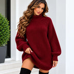 A woman wearing an oversized ribbed knit turtleneck sweater in deep burgundy, paired with black thigh-high socks, standing in front of a white architectural background with a green plant.