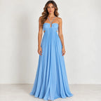A woman modeling a light blue sleeveless maxi dress with a sweetheart neckline, thin crisscross straps, side cutouts, and a flowing pleated skirt against a plain off-white studio background.