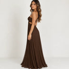 A woman modeling a floor-length brown strapless gown with side cutouts and a flowing pleated skirt, photographed against a plain light gray studio background.