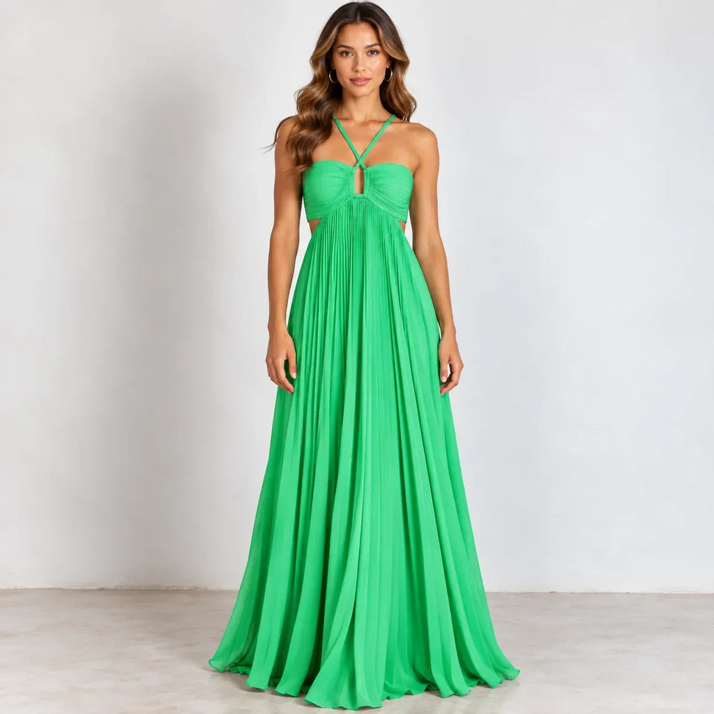 A woman modeling a bright green floor-length halter gown with a fitted bodice, side cutouts, and a flowing pleated skirt against a plain light gray studio background.