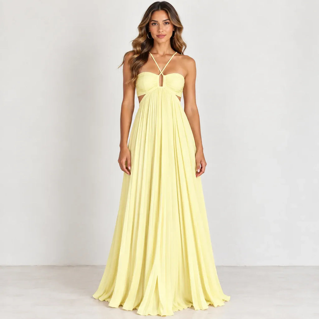 A woman modeling a pale yellow strapless maxi dress with a sweetheart neckline, thin crossover halter straps, side cutouts, and a flowing pleated skirt against a plain light gray studio background.