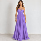 A woman modeling a floor-length lavender purple halter-neck gown with a sweetheart neckline, gathered bodice, and flowing pleated skirt, standing against a plain light gray wall.