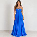 A woman modeling a bright royal blue floor-length gown with a halter-style neckline, front cutout detail, and flowing pleated skirt against a plain light gray studio background.