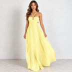 A woman modeling a bright yellow strapless maxi dress with thin crossover halter straps, a sweetheart neckline, and a flowing pleated skirt, standing against a plain light gray studio background.