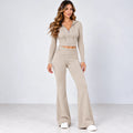 A woman modeling a matching beige two-piece lounge set consisting of a cropped zip-up hoodie with long sleeves and high-waisted flared pants, paired with white sneakers, against a light gray studio background.