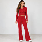 A woman modeling a matching red two-piece set consisting of a cropped zip-up hoodie with drawstrings and high-waisted flared pants, photographed against a plain light gray studio background.