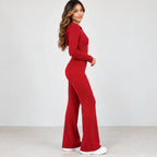 A woman modeling a bright red long-sleeve jumpsuit with a high neckline and wide-leg flared pants, paired with white sneakers, against a plain light gray studio background.