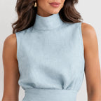 A close-up of a woman wearing a light blue sleeveless mock-neck top or dress bodice, shown against a plain light background.