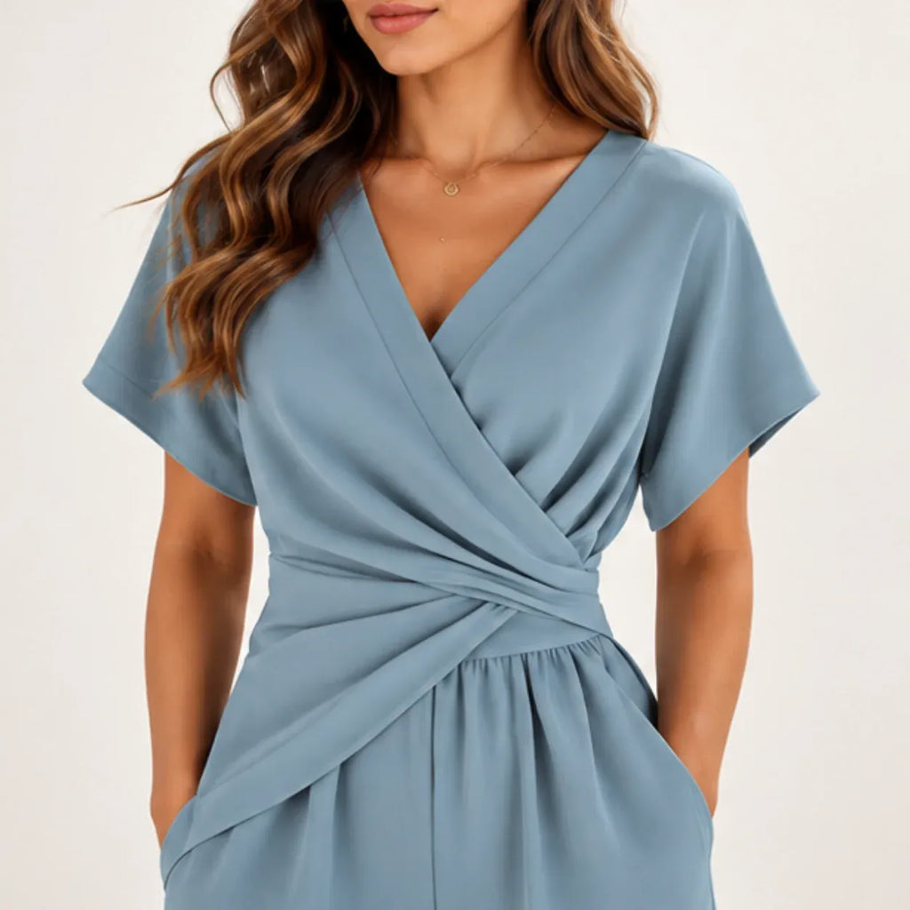 A woman wearing a light blue wrap-style dress with short sleeves and a twisted waist detail, shown against a plain light background.