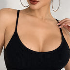 Close-up of a woman wearing a black ribbed scoop-neck bralette with thin straps and large hoop earrings against a light gray background.