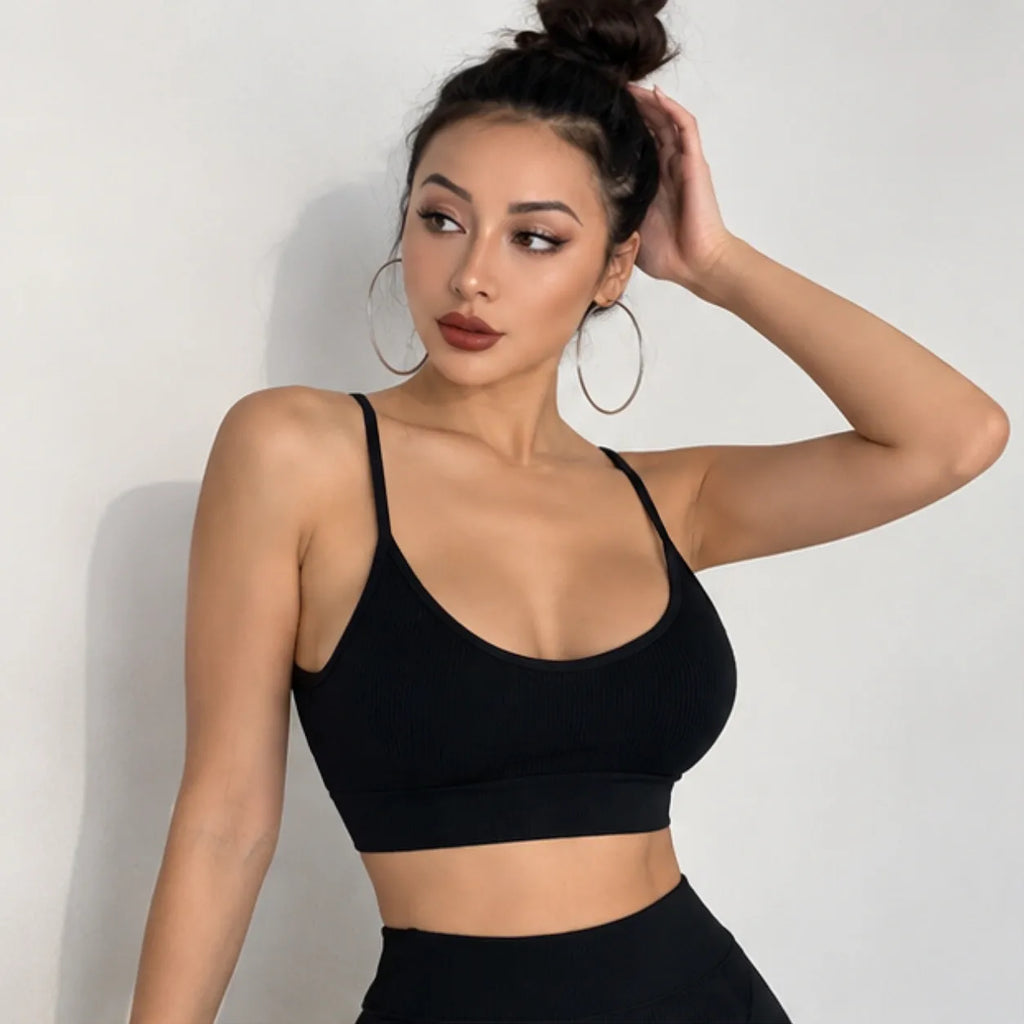 A woman wearing a black ribbed sports bra and matching black high-waisted leggings, posing against a plain light gray wall.