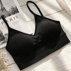 A black ribbed wireless bra with a V-neckline and thin adjustable straps, styled on a white wooden surface next to a Paris magazine and dried flowers.