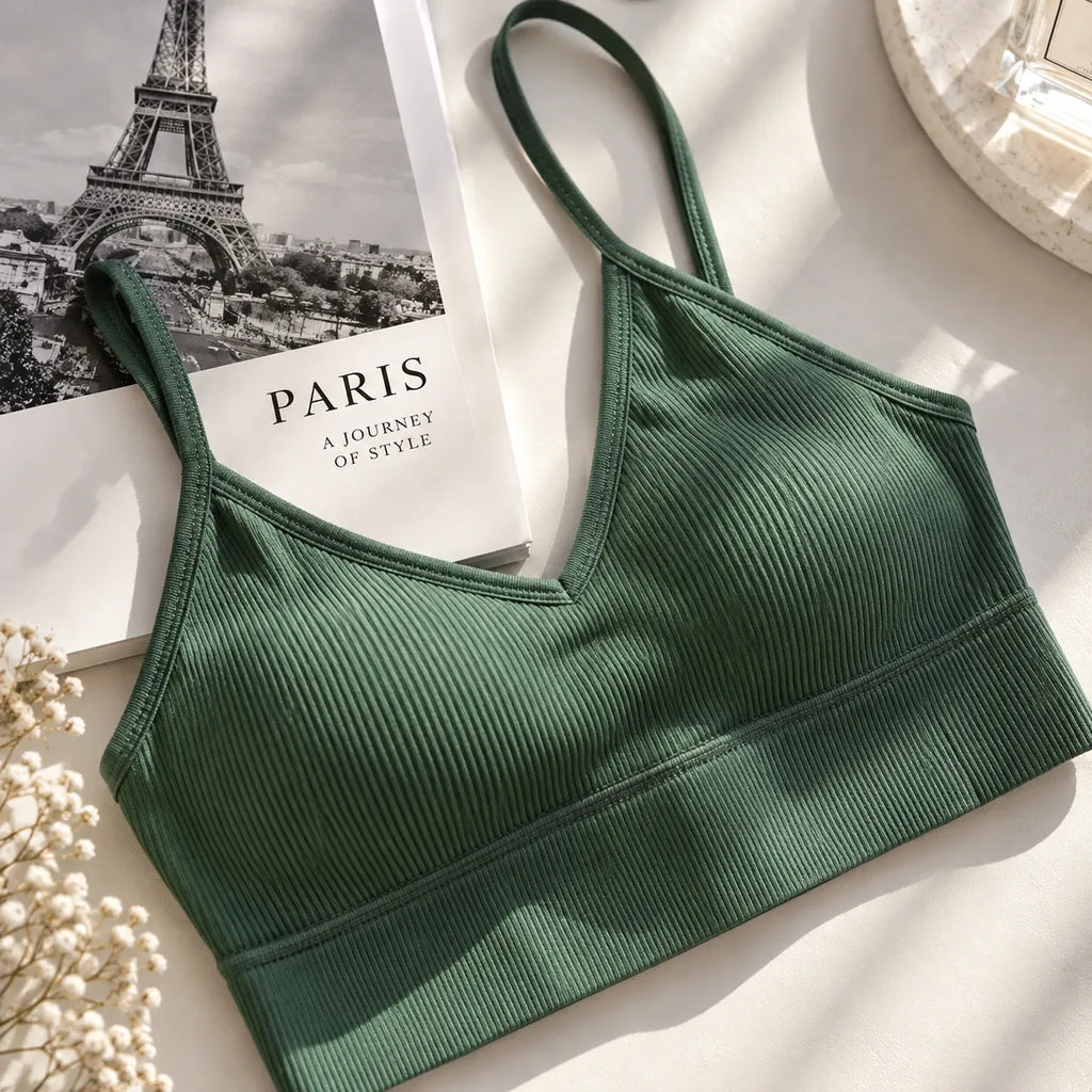 A dark green ribbed sports bra with thin straps, styled on a white surface next to a Paris-themed book, dried flowers, and a decorative tray.