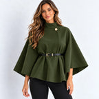 A woman modeling an olive green cape-style top with a single gold button, a matching black belt with a gold buckle, and black pants, set against a plain light gray background.