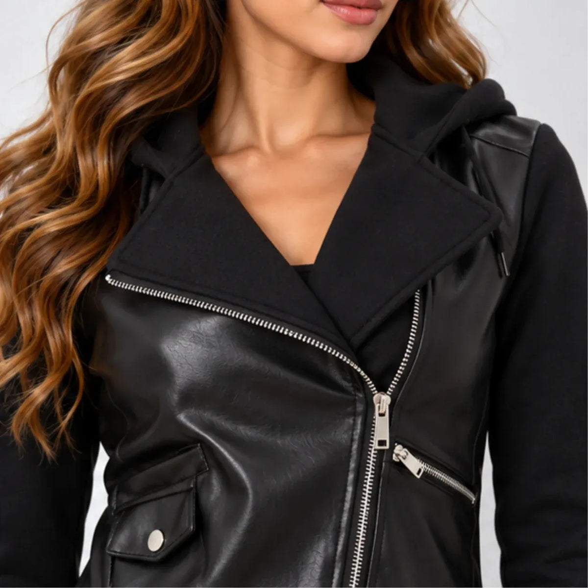 A close-up of a woman wearing a black faux-leather moto jacket with a hood and silver zipper, paired with a black hoodie underneath.