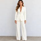 A woman modeling a matching off-white tailored pantsuit with a single-breasted blazer and wide-leg trousers, standing against a plain light gray wall.