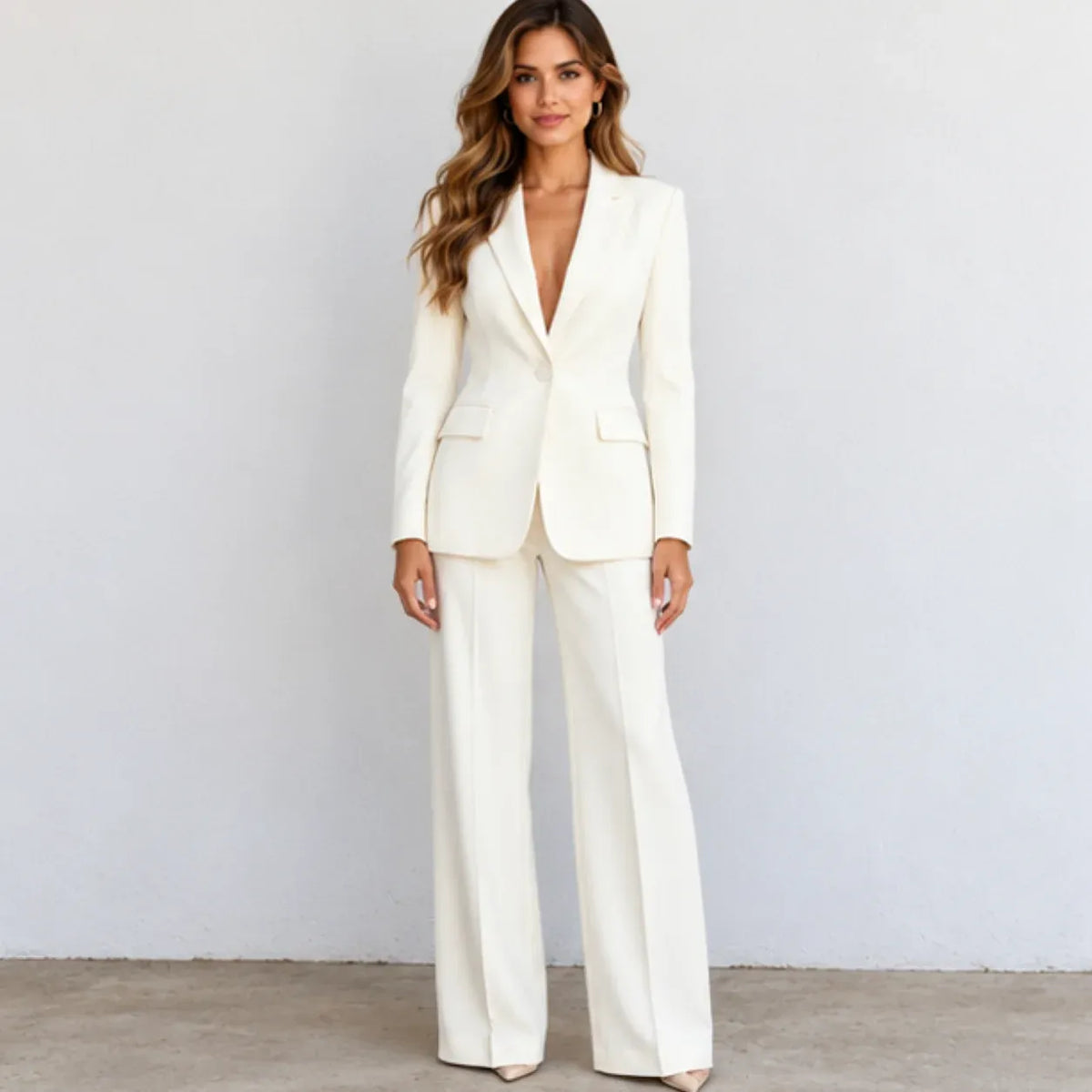 A woman modeling a matching off-white tailored pantsuit with a single-breasted blazer and wide-leg trousers, standing against a plain light gray wall.