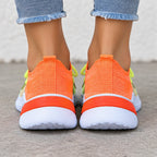 A close-up rear view of a person wearing bright orange and white athletic sneakers with light blue frayed-hem jeans, standing on a concrete surface.
