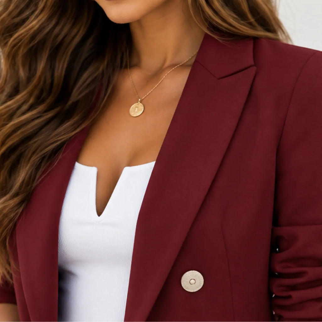 A close-up of a woman wearing a burgundy blazer over a white V-neck top, accessorized with a gold pendant necklace.