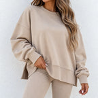 A woman wearing a beige crewneck sweatshirt and matching ribbed leggings, shown from the neck down against a light textured wall.