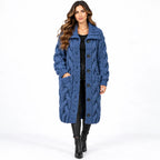A woman modeling a long, chunky cable-knit blue coat with large buttons and front pockets, worn over a black outfit against a plain white studio background.