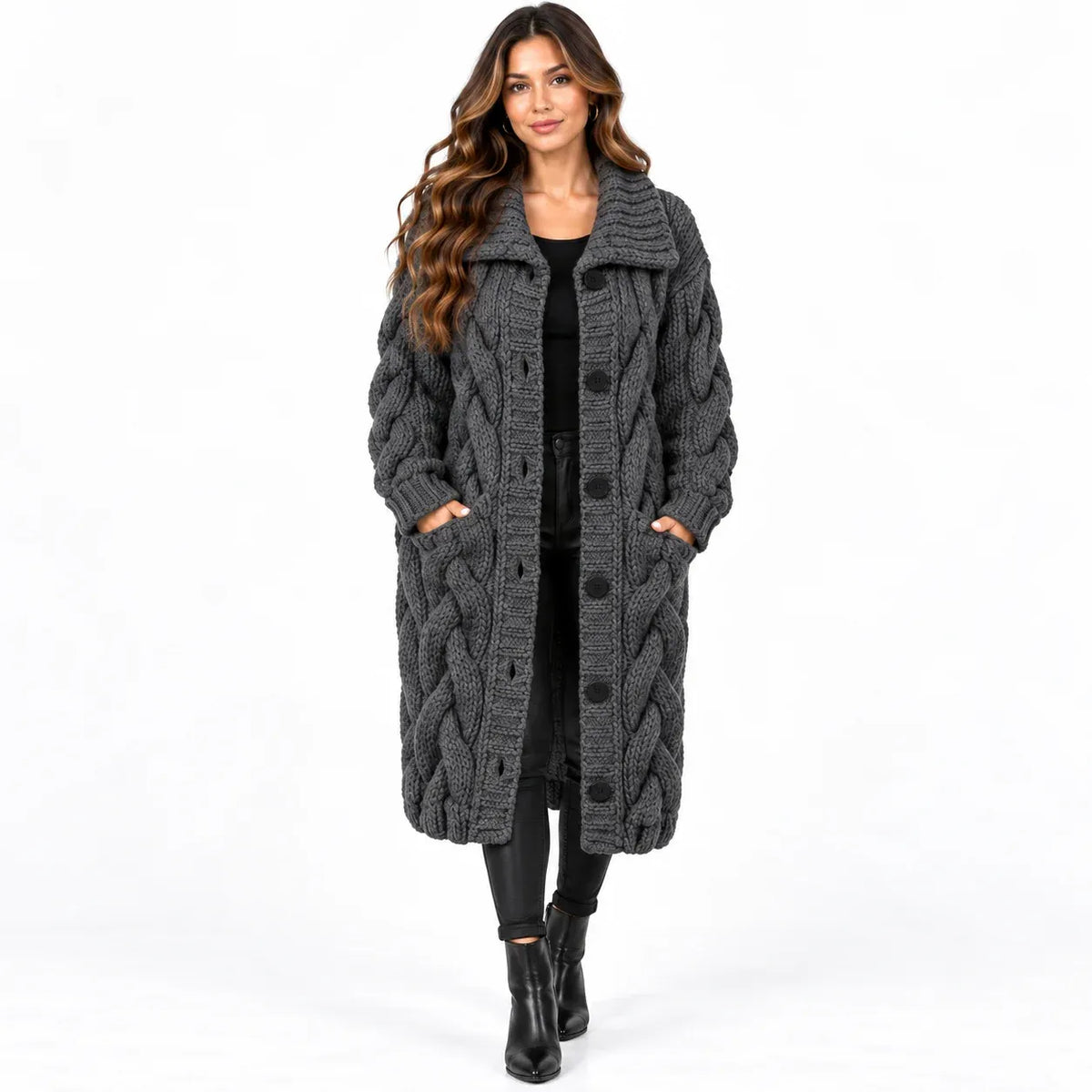 A woman modeling a long, dark gray cable-knit coat with large buttons and side pockets, worn over a black outfit against a plain white background.