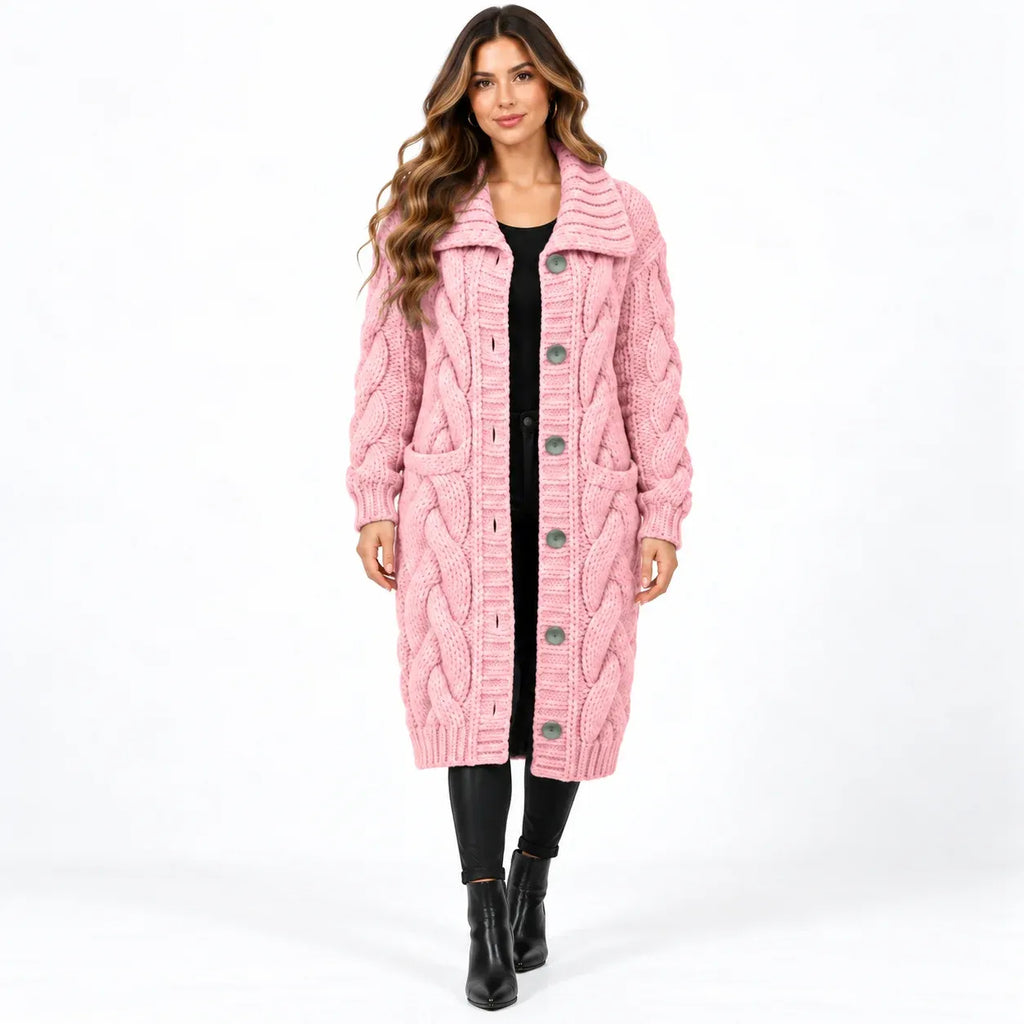 A woman modeling a pink cable-knit long cardigan with a high ribbed collar, front button closure, and large front pockets, worn over a black outfit on a white studio background.