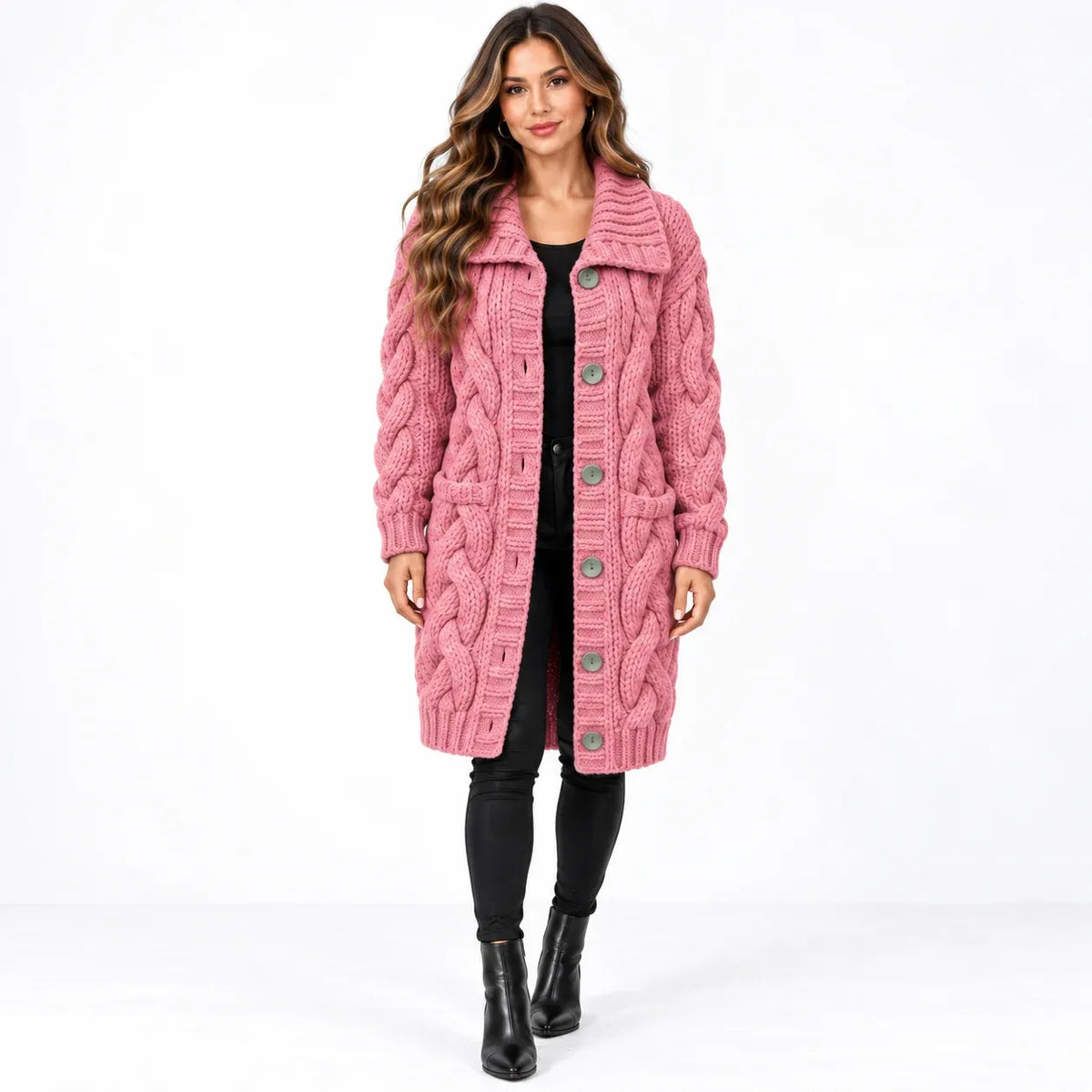 A woman modeling a pink cable-knit button-front coat with large front pockets, worn over a black outfit and black ankle boots against a plain white studio background.