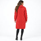 A woman viewed from the back wearing a bright red cable-knit long coat with a high collar, paired with black leggings and black ankle boots, against a plain white studio background.
