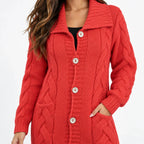 A woman wearing a red cable-knit cardigan sweater with a wide collar and large buttons, shown from the neck down against a plain white background.