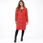 A woman modeling a red cable-knit coat with a wide collar and front buttons, paired with black pants and black ankle boots, against a plain white studio background.