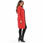 A woman modeling a red cable-knit long coat with large buttons, worn over a black outfit and black ankle boots, against a plain white studio background.