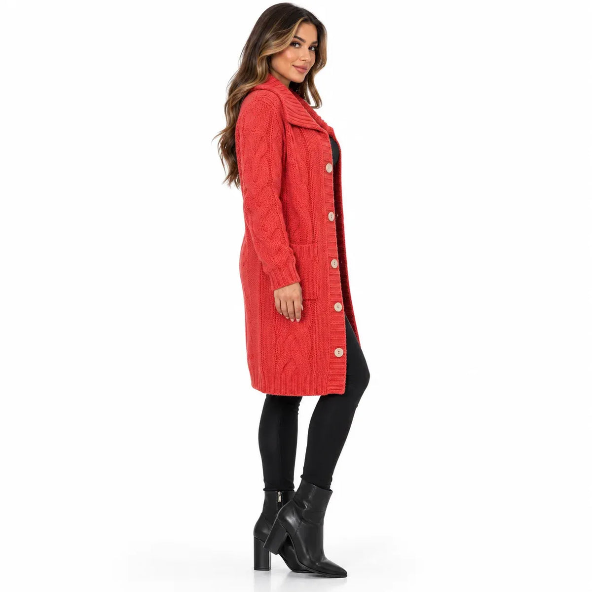 A woman modeling a red cable-knit long coat with large buttons, worn over a black outfit and black ankle boots, against a plain white studio background.