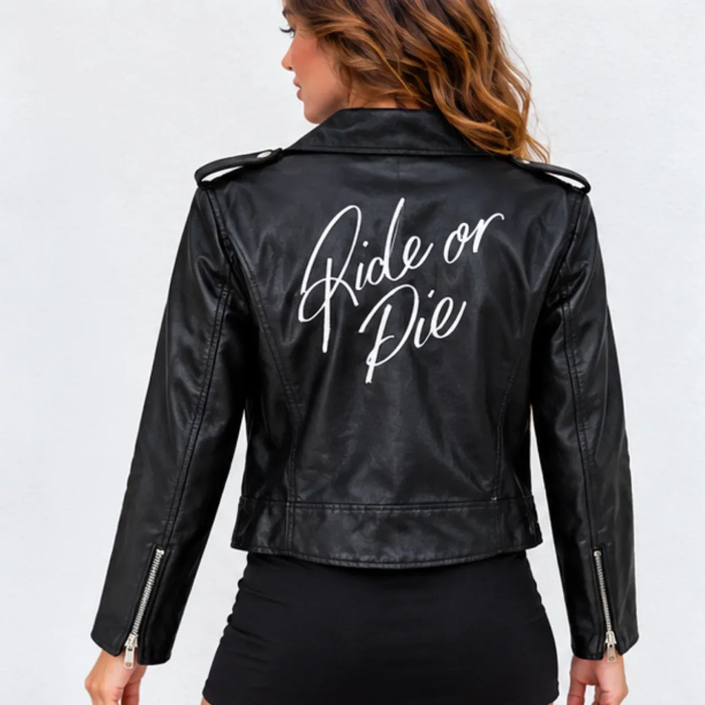 A woman shown from the back wearing a black faux-leather moto jacket with 'Ride or Die' printed in white script across the back. The jacket features silver zipper details on the sleeves and shoulder epaulets.