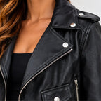 Close-up of a woman wearing a black faux-leather moto jacket with silver-tone snap and zipper details over a black top.
